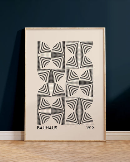 Innrammað Bauhaus veggspjald, upp við dökkbláan vegg, ofan á viðargólfi