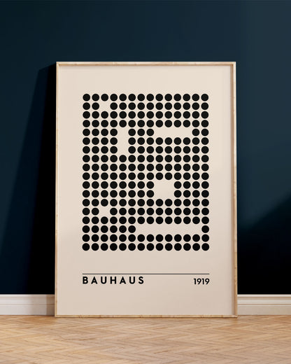 Innrammað Bauhaus veggspjald, uppvið bláan vegg, ofan á brúnu viðargólfi.