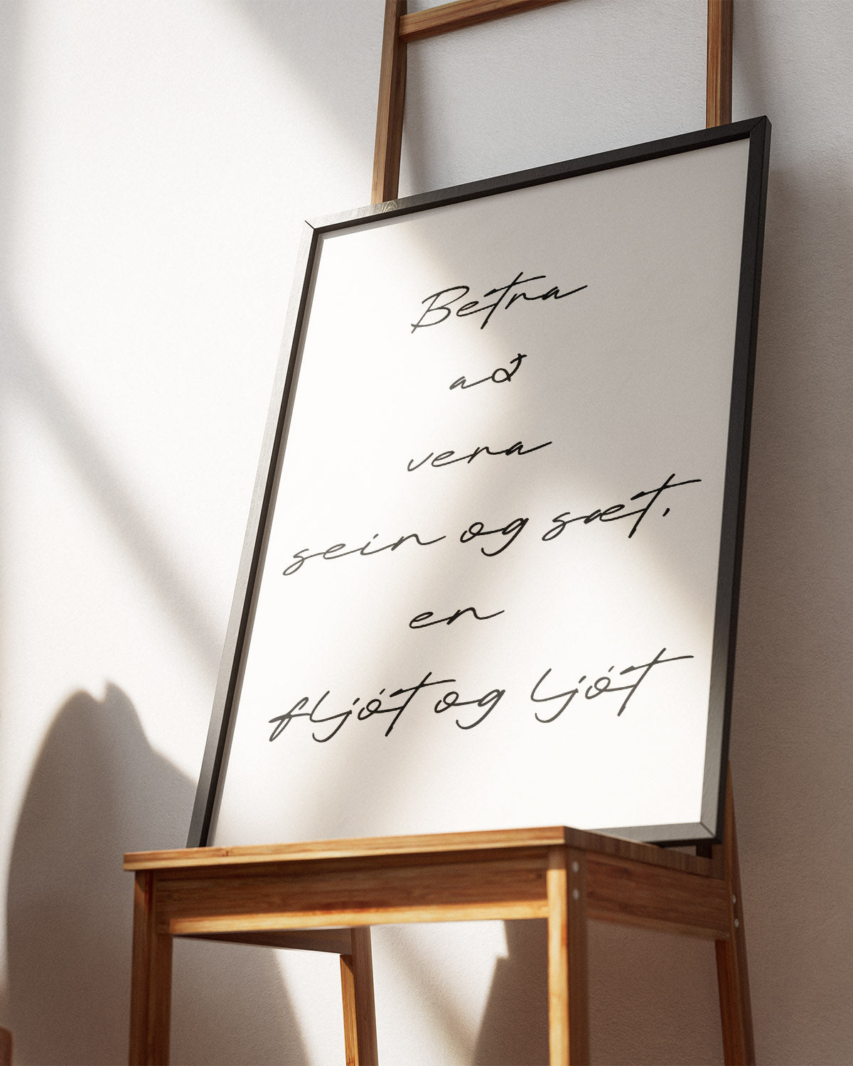 Veggspjald í svörtum ramma á stól með textanum: Betra að vera sein og sæt, en fljót og ljót